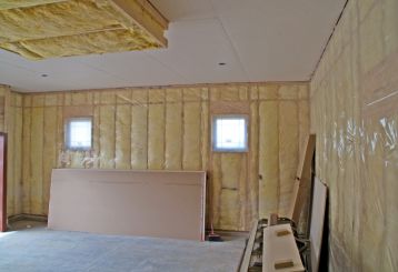Garage interior with yellow insulation installed on walls and ceiling, drywall sheets stacked, and construction materials visible