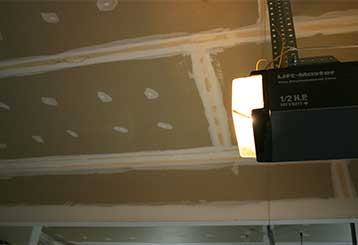 Illuminated garage door opener unit mounted in a residential garage, representing professional garage door opener replacement and enhanced home security.