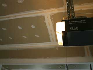 Garage Door Opener Replacement – Professional Installation Example Illuminated garage door opener unit mounted in a residential garage, representing professional garage door opener replacement and enhanced home security.