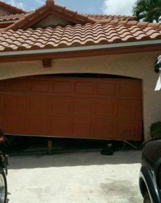 Front view of a garage door leaning diagonally due to spring failure, awaiting emergency repair in Tukwila